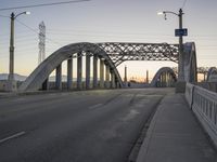 a bridge with a light post, an overhead street lamp and poles that are tall