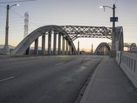 a bridge with a light post, an overhead street lamp and poles that are tall