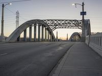 a bridge with a light post, an overhead street lamp and poles that are tall