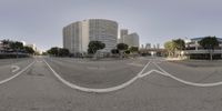 a photo of a street intersection, with several white painted lines down the road and the buildings are tall behind it