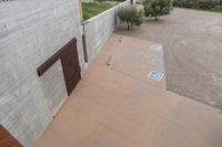 a parking spot with painted lines is near a building by the river bank near an olive tree