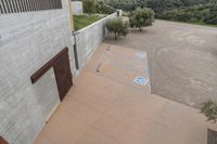 a parking spot with painted lines is near a building by the river bank near an olive tree