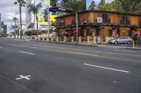 the view of a city street lined with parked cars and restaurants along side of the road