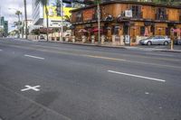 the view of a city street lined with parked cars and restaurants along side of the road