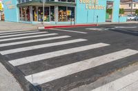 a cross walk crossing the road in front of a store on a corner with a blue building