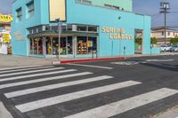 a cross walk crossing the road in front of a store on a corner with a blue building