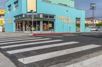 a cross walk crossing the road in front of a store on a corner with a blue building