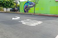 a painted mural of a chamelon is next to a closed street with two trees in the foreground and an arrow indicating the intersection