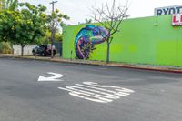 a painted mural of a chamelon is next to a closed street with two trees in the foreground and an arrow indicating the intersection