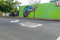 a painted mural of a chamelon is next to a closed street with two trees in the foreground and an arrow indicating the intersection