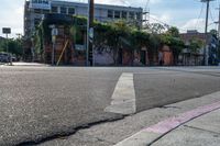 the empty street is busy with cars and shops in the background, the man with a skateboard is crossing the intersection