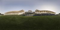 an empty baseball stadium sitting next to the green grass lawn in the day time,