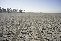 people walk on sand at a beach, near the ocean in the distance is a sky with few cloudless, and blue skies