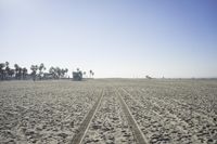 people walk on sand at a beach, near the ocean in the distance is a sky with few cloudless, and blue skies