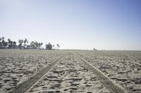 people walk on sand at a beach, near the ocean in the distance is a sky with few cloudless, and blue skies