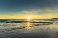 a sunset seen from the shoreline of a beach with waves and mountains in the distance