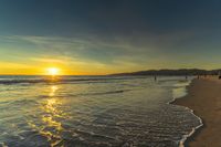 a sunset seen from the shoreline of a beach with waves and mountains in the distance