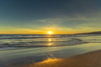 a sunset seen from the shoreline of a beach with waves and mountains in the distance