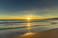 a sunset seen from the shoreline of a beach with waves and mountains in the distance