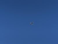 an airplane flying in the clear blue sky in a city park area, with a plane taking off in the distance