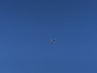 an airplane flying in the clear blue sky in a city park area, with a plane taking off in the distance