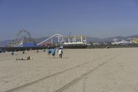 people walk on sand at a beach, near the ocean in the distance is a sky with few cloudless, and blue skies