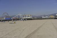 people walk on sand at a beach, near the ocean in the distance is a sky with few cloudless, and blue skies