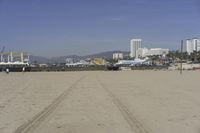 people walk on sand at a beach, near the ocean in the distance is a sky with few cloudless, and blue skies