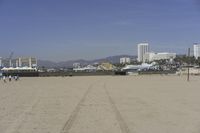 people walk on sand at a beach, near the ocean in the distance is a sky with few cloudless, and blue skies