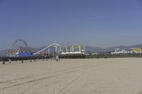 people walk on sand at a beach, near the ocean in the distance is a sky with few cloudless, and blue skies