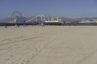 people walk on sand at a beach, near the ocean in the distance is a sky with few cloudless, and blue skies