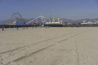 people walk on sand at a beach, near the ocean in the distance is a sky with few cloudless, and blue skies