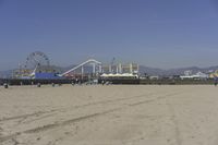 people walk on sand at a beach, near the ocean in the distance is a sky with few cloudless, and blue skies