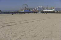 people walk on sand at a beach, near the ocean in the distance is a sky with few cloudless, and blue skies