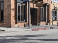 the motorcycle is stopped near the brick building on the street corner beside the curb, and with one leg visible