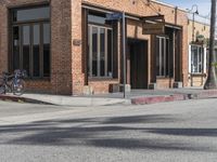 the motorcycle is stopped near the brick building on the street corner beside the curb, and with one leg visible