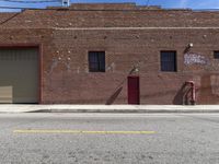 an empty street in front of a brick building with two garages on both side and a red fire hydrant in the distance