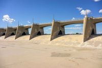 a bridge that is over the water in a desert area with sand on either side