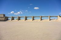 cement bridge overpass on dirt field under cloudy blue sky, with water flowing below