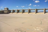 cement bridge overpass on dirt field under cloudy blue sky, with water flowing below