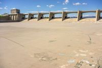 cement bridge overpass on dirt field under cloudy blue sky, with water flowing below