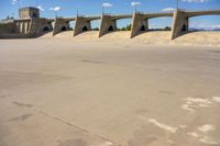 cement bridge overpass on dirt field under cloudy blue sky, with water flowing below