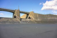 a skate board sitting on top of a concrete ramp below a bridge with a concrete structure