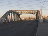 a big metal bridge over a freeway with buildings in the background and water in the foreground