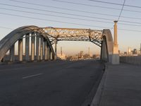 a big metal bridge over a freeway with buildings in the background and water in the foreground