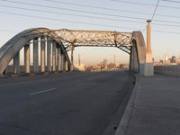 a big metal bridge over a freeway with buildings in the background and water in the foreground