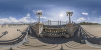 a 360 - angle photo of a bridge over looking water and some streetlights with clouds in the background