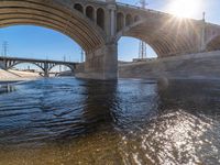 a river with some rocks in it under a bridge above water and with power lines