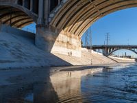 a river runs underneath the large bridge with water in between it and people walking below the bridge