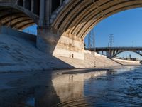 a river runs underneath the large bridge with water in between it and people walking below the bridge